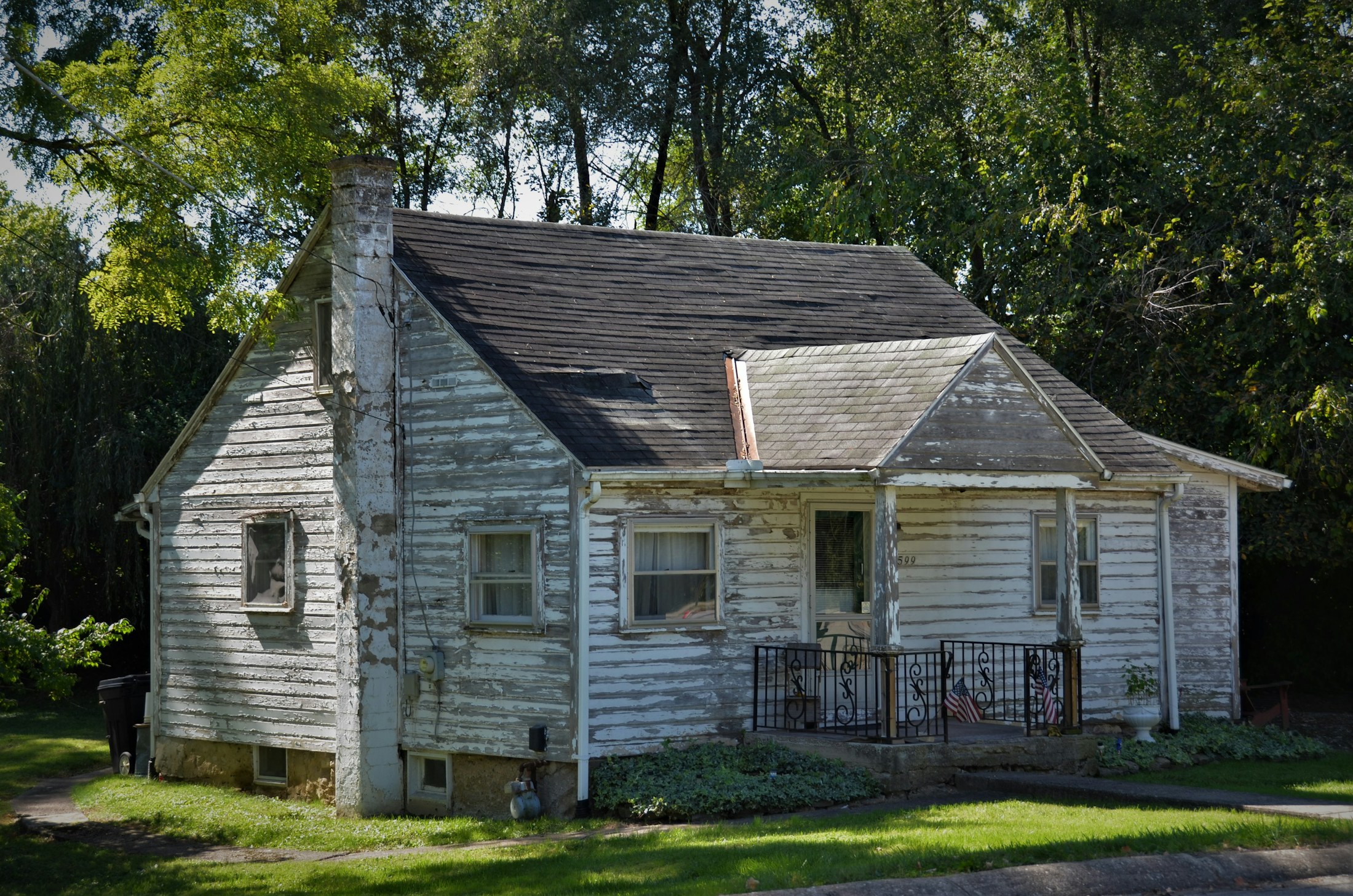 Weathered white house with peeling paint and an unobstructed front porch.